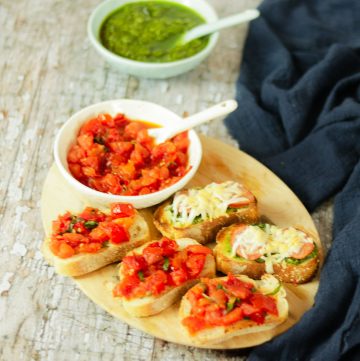 platter of bruschetta with tomato topping and bowl of pesto