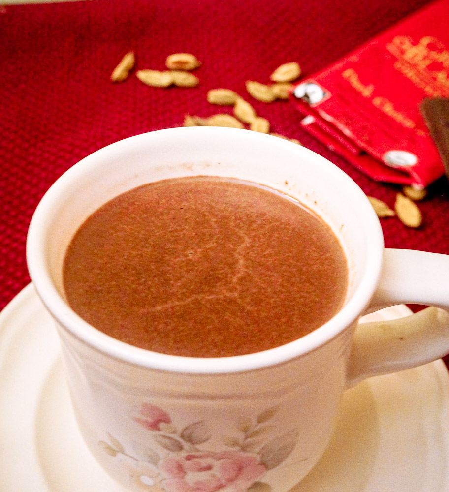 mug of hot cocoa with cardamom and chocolate in the background