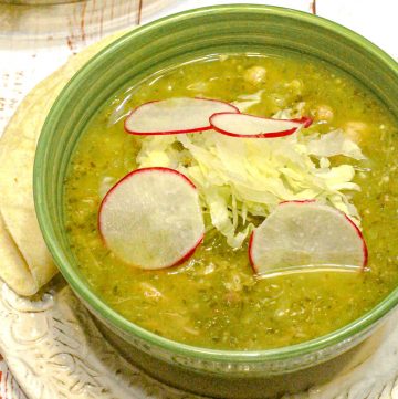 bowl of pozole soup garnished with cabbage and sliced radish in a green bowl on a white plate