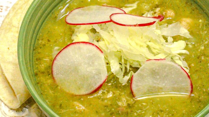 bowl of pozole soup garnished with cabbage and sliced radish in a green bowl on a white plate