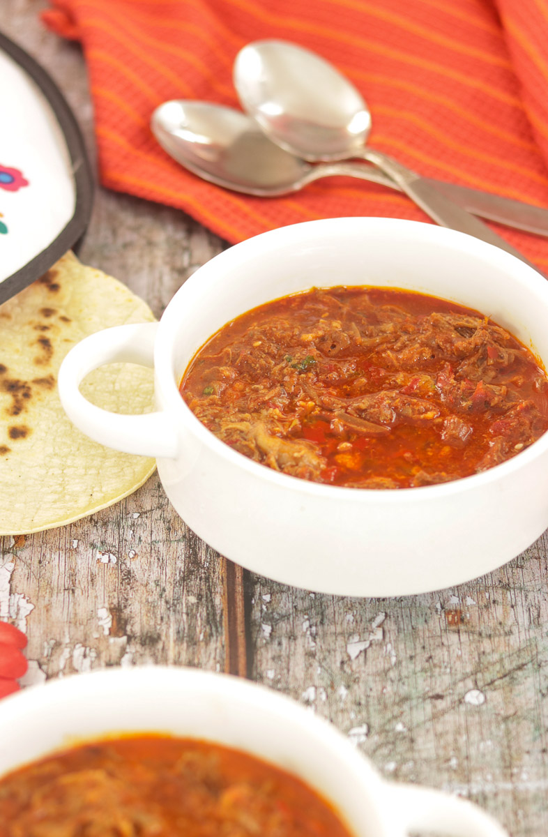 bowls of birria consome with spoons