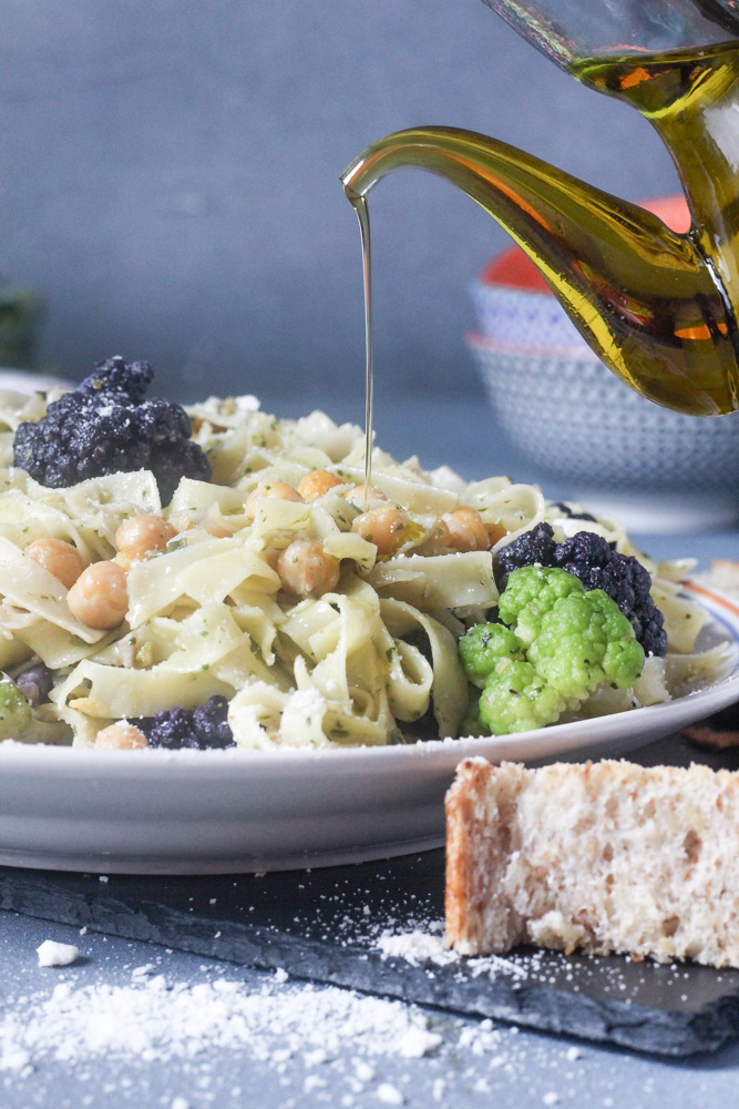 Platter of pasta and cauliflower with olive oil drizzled over plate and piece of bread.