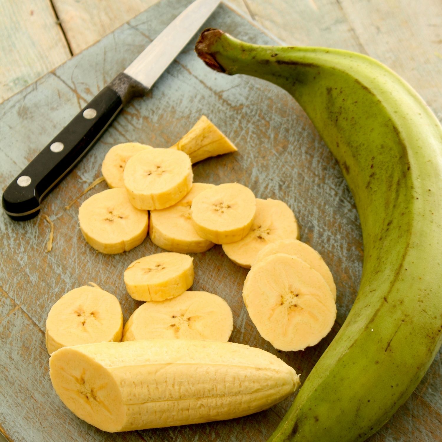 how to peel and cook plantains - Green plantain on a cutting board with plantain slices and a knife