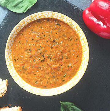 bowl of red pepper pesto with bell pepper and basil leaf.