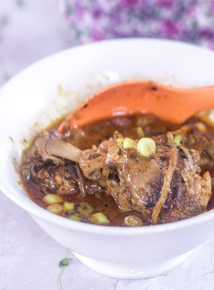 Haitian Stew Chicken with orange serving spoon in a bowl,