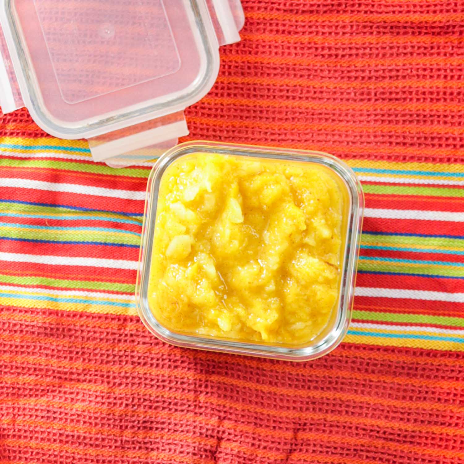 Mango Applesauce in a bowl on a bright colored kitchen towel.