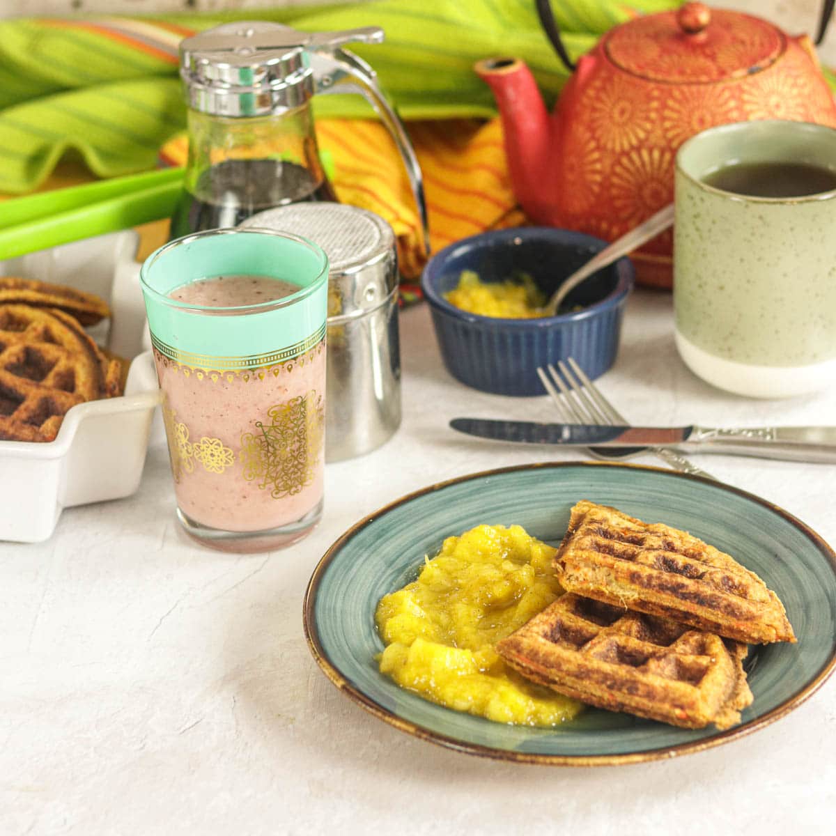 Healthy Whole Wheat Waffles with Mango Applesauce on a plate with breakfast accoutrements in the background.