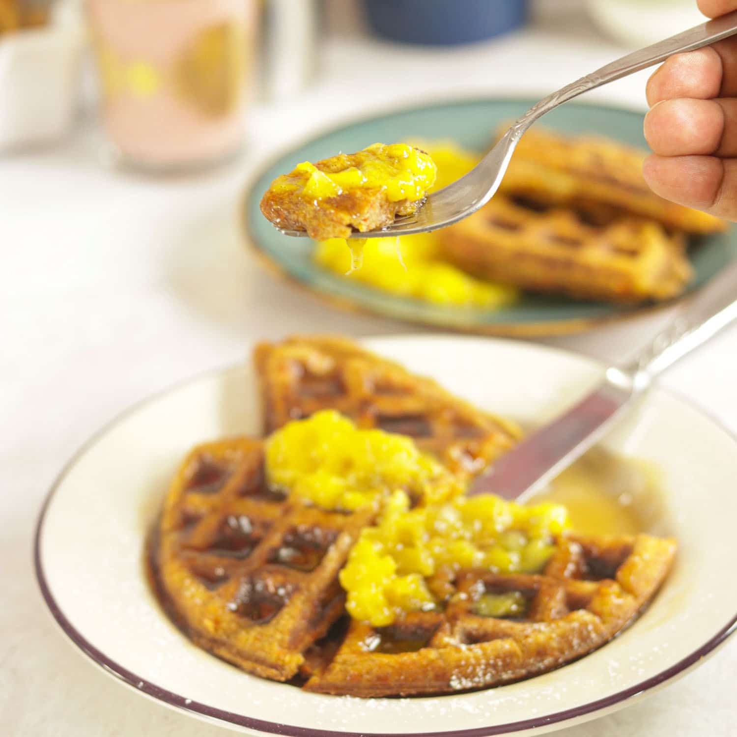 Carrot Waffles with Mango Applesauce and Syrup on a fork with breakfast plates in the background