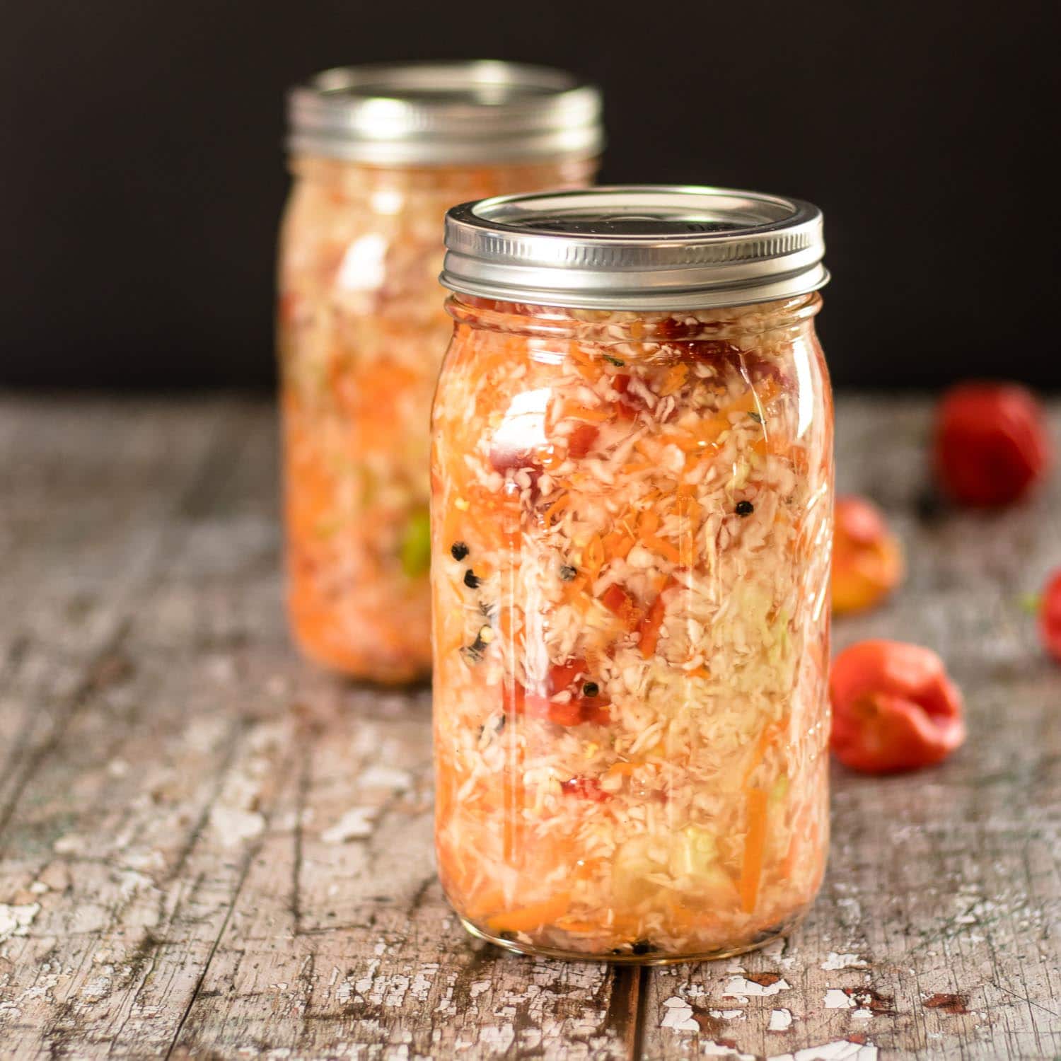 Haitian Pikliz recipe in Mason Jars with Scotch Bonnet peppers in the background