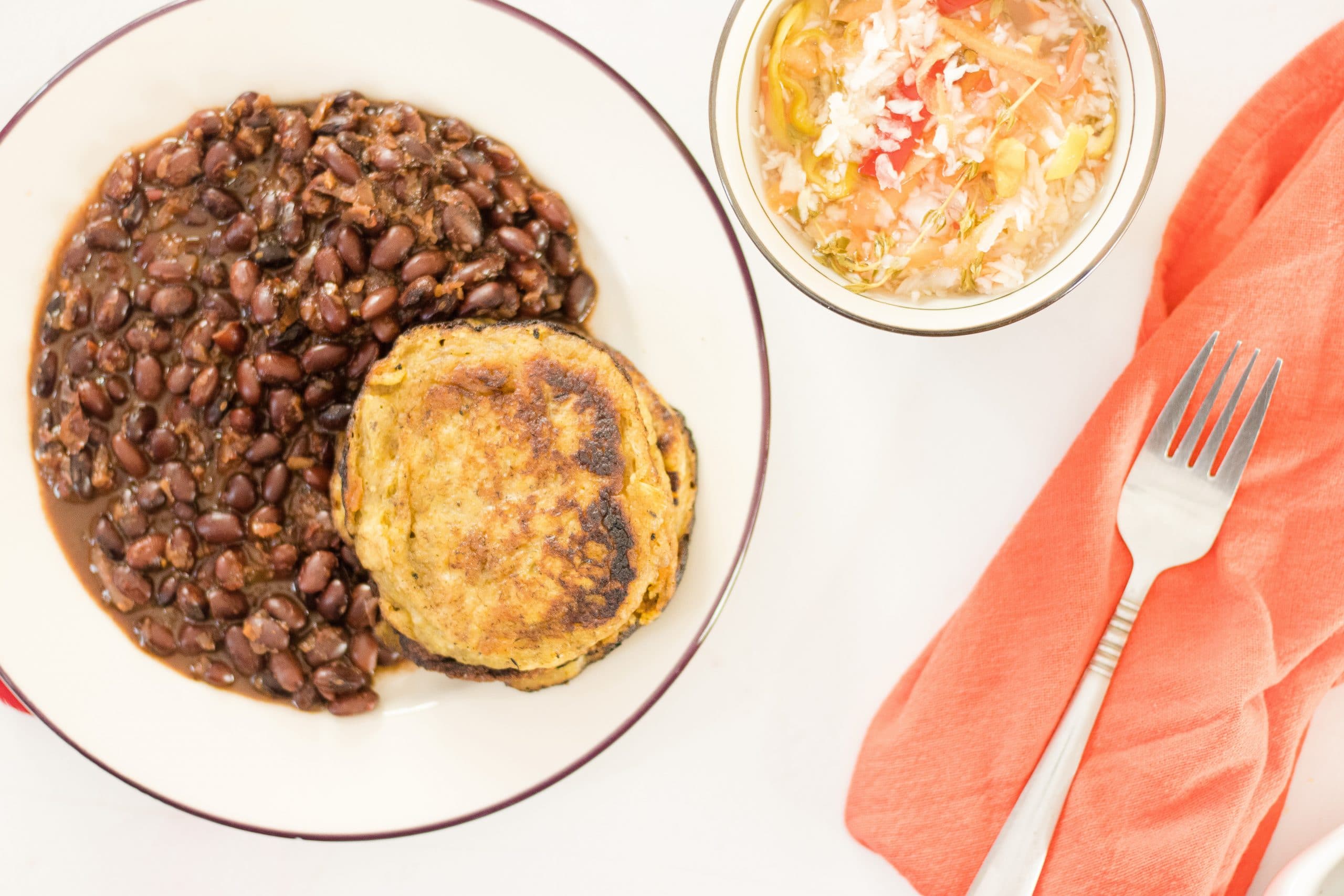 Tatale Plantain Pancakes on a plate with beans and pikliz in a bowl.