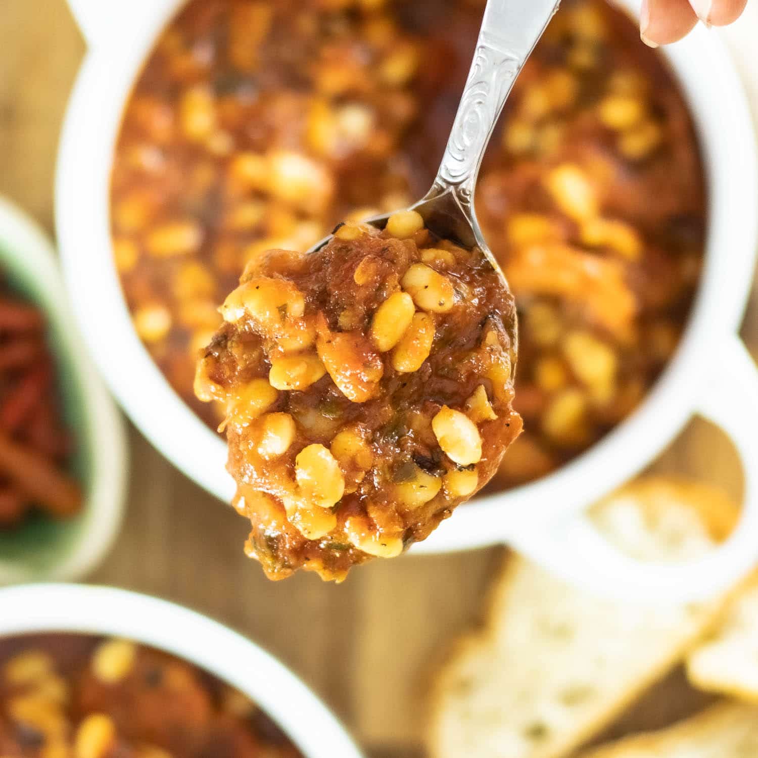 White bean stew on a spoon with bowls and bread in background