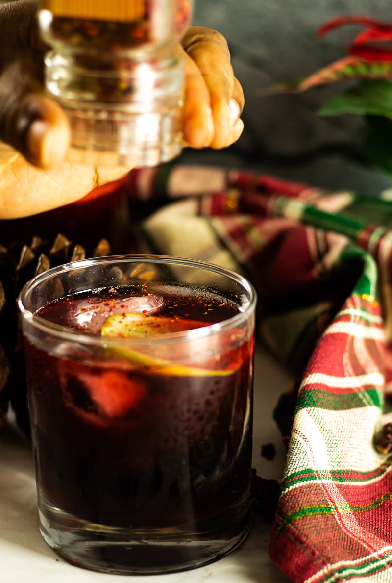 Hibiscus Christmas Punch with Pink Peppercorn garnisha nd christmas decorations in background