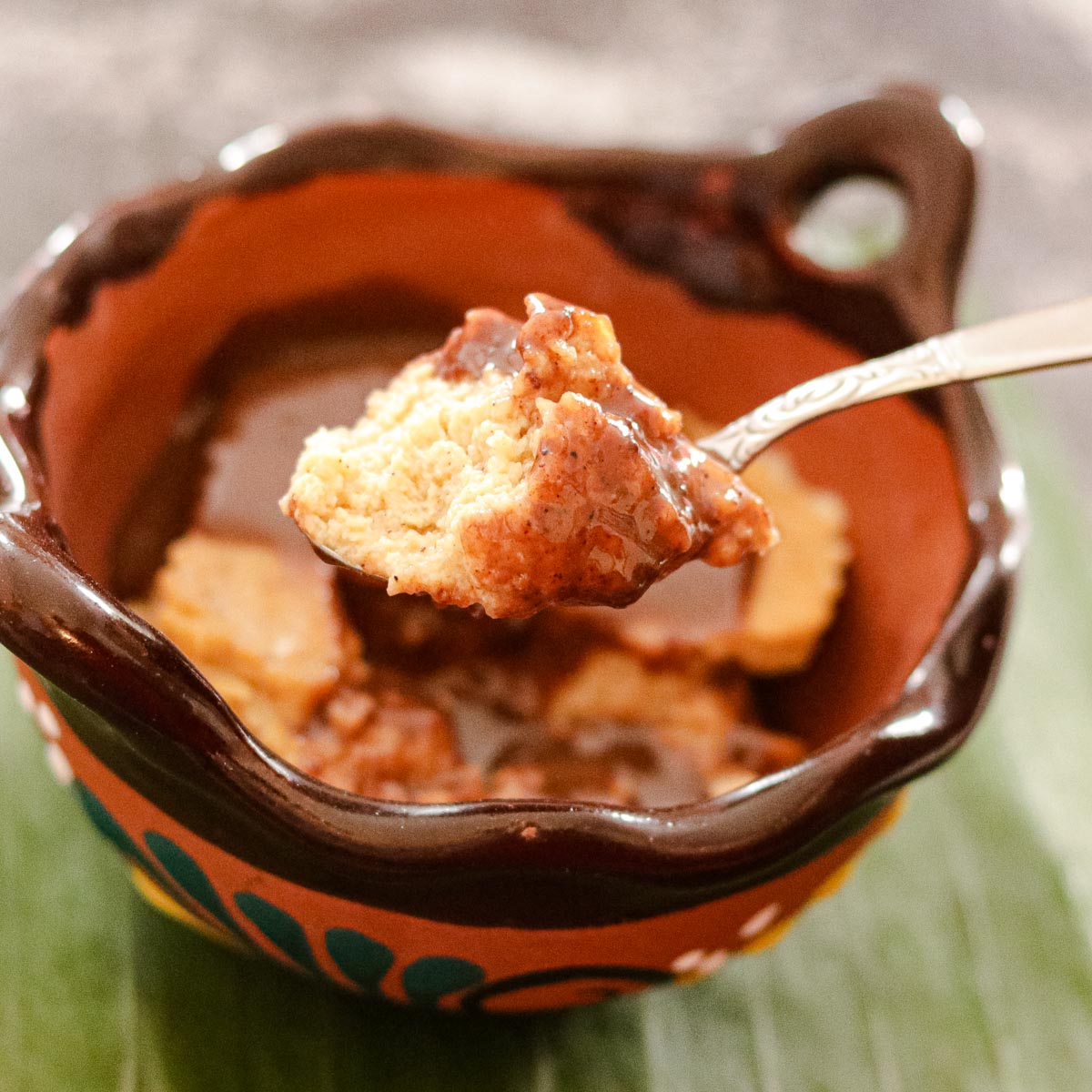 champurrado custard on a spoon with chocolate sauce over a bowl