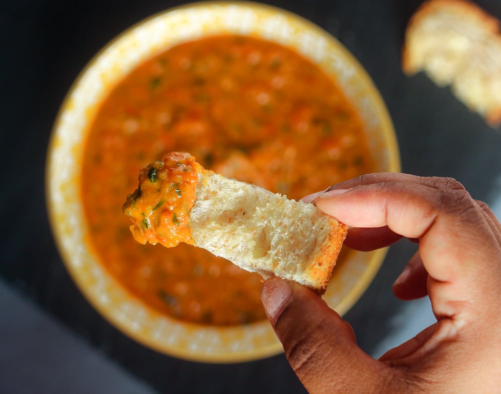 red pepper pesto on a piece of bread being held by a hand