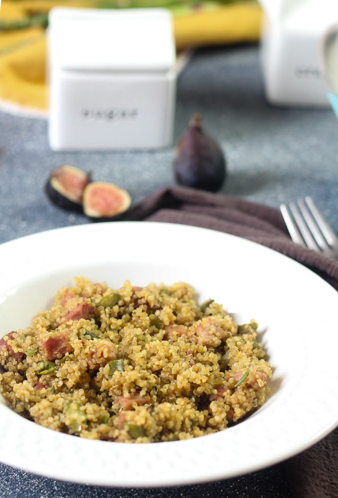 bowl of cooked quinoa with ham and asparagus with fresh figs in the background