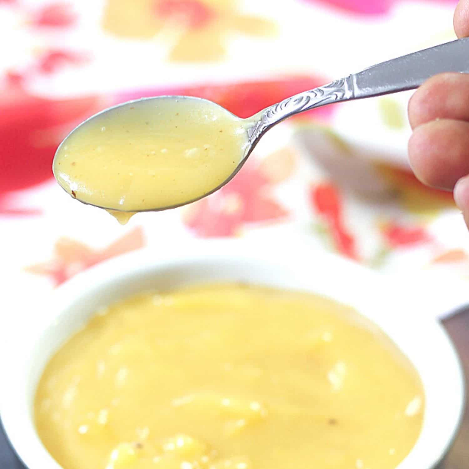 Lemon Curd on a spoon over a bowl filled with lemon curd.