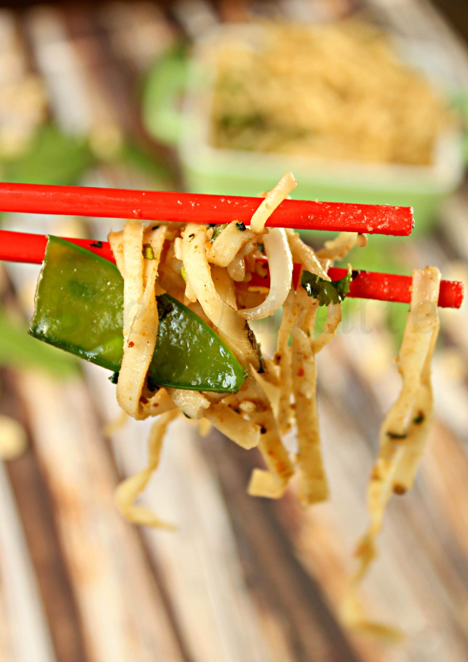 Sesame Peanut Noodles with Snow peas being held by chopsticks