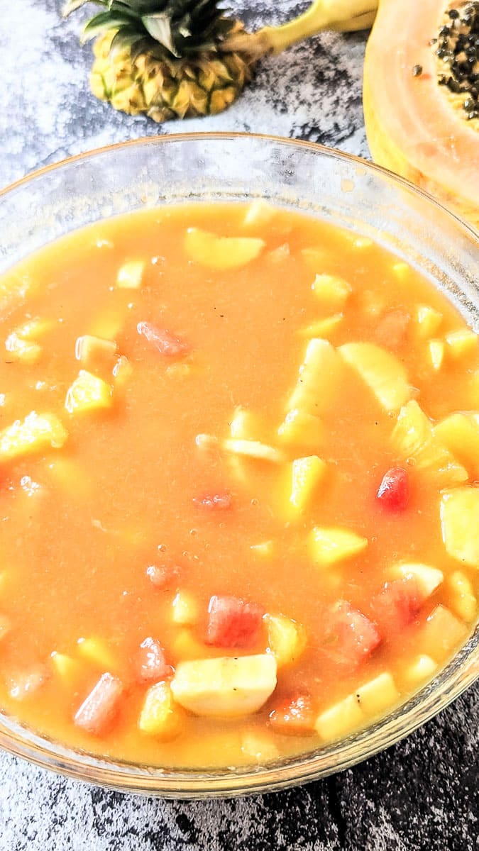 Tropical Fruit Punch in a punch bowl with papaya and pineapple top in the background